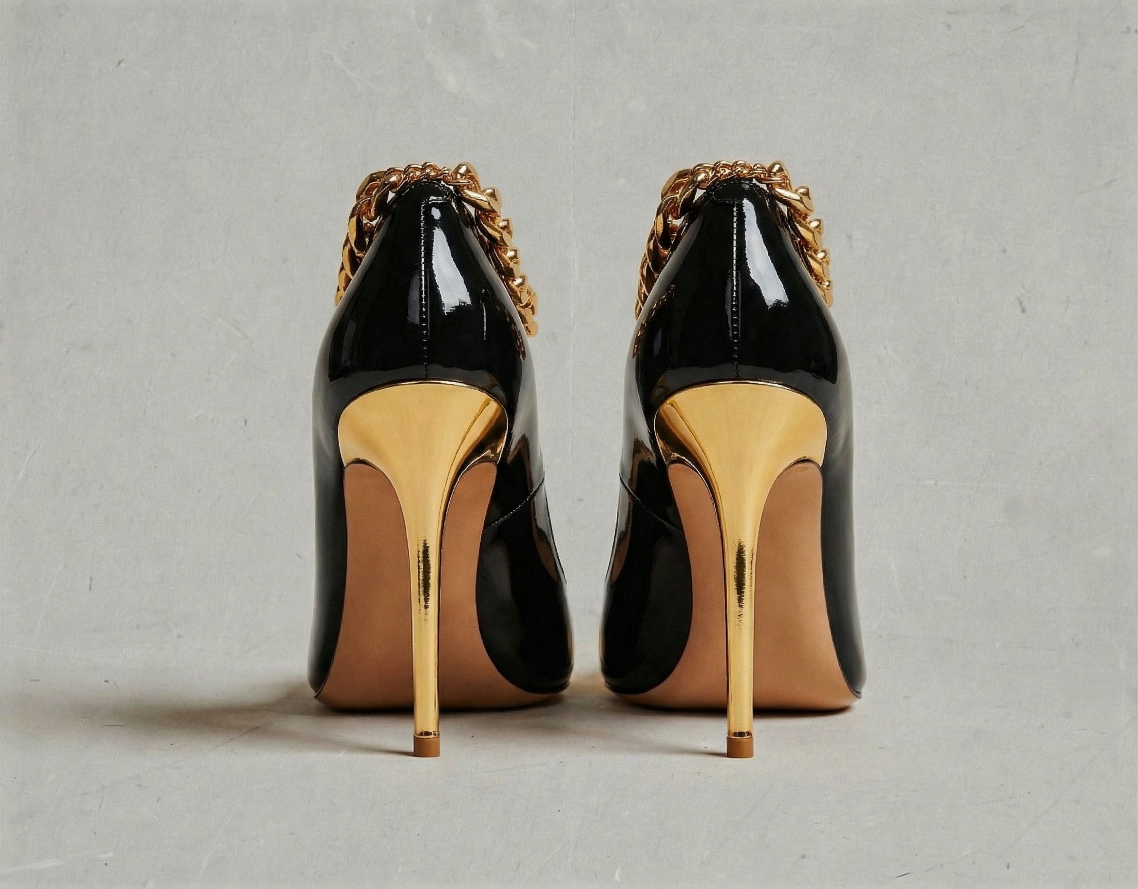 Black high-heeled shoes with gold accents on a gray background