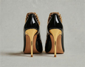 Black high-heeled shoes with gold accents on a gray background