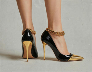 Black high-heeled shoes with gold accents and chain details on a neutral background