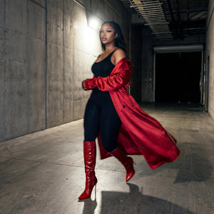 Woman in a red coat and boots standing in a dimly lit hallway.