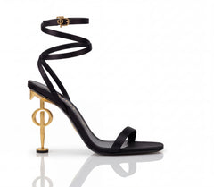 Black high-heeled sandal with gold heel and strap design on a white background