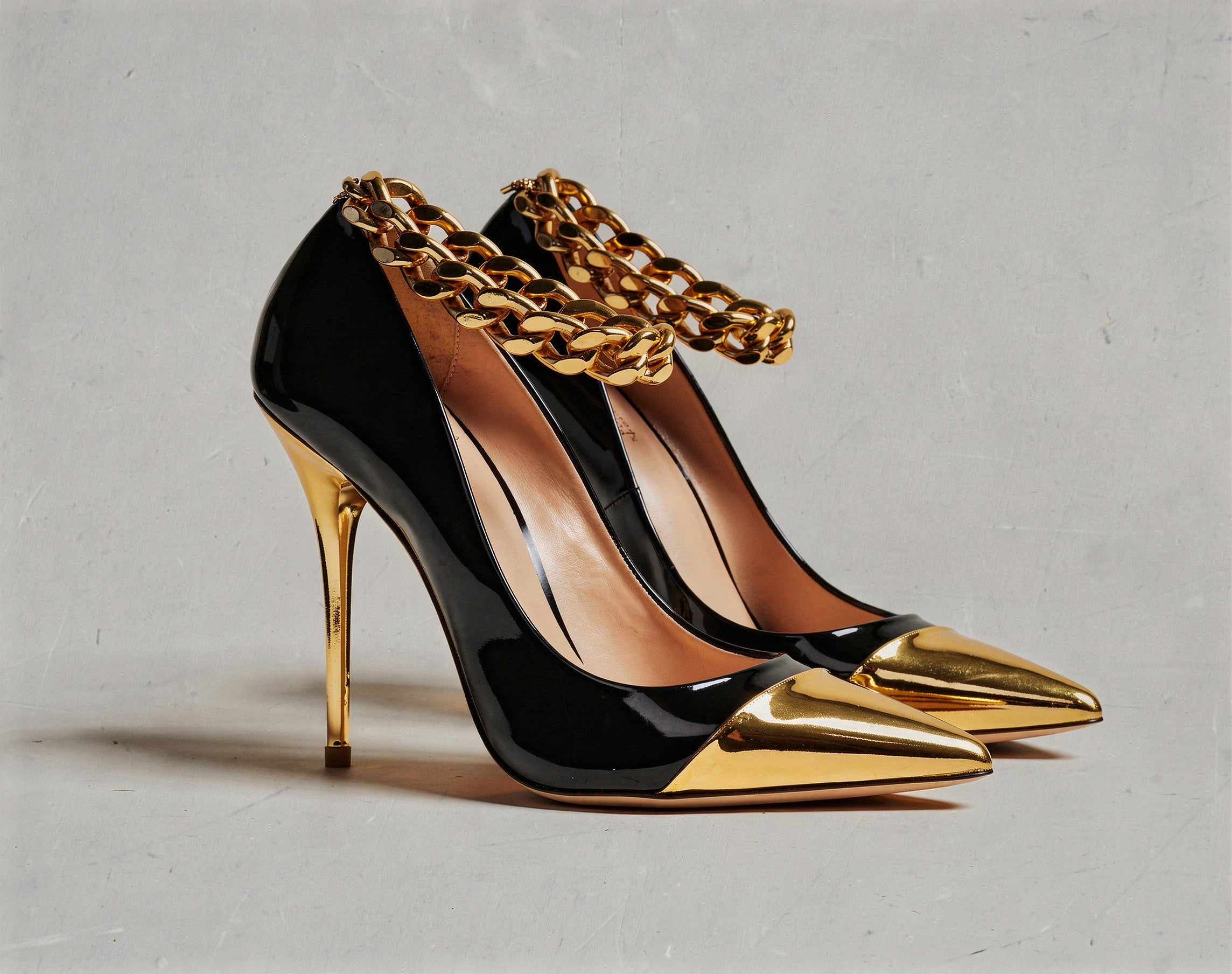 Black high-heeled shoes with gold accents and chains on a gray background