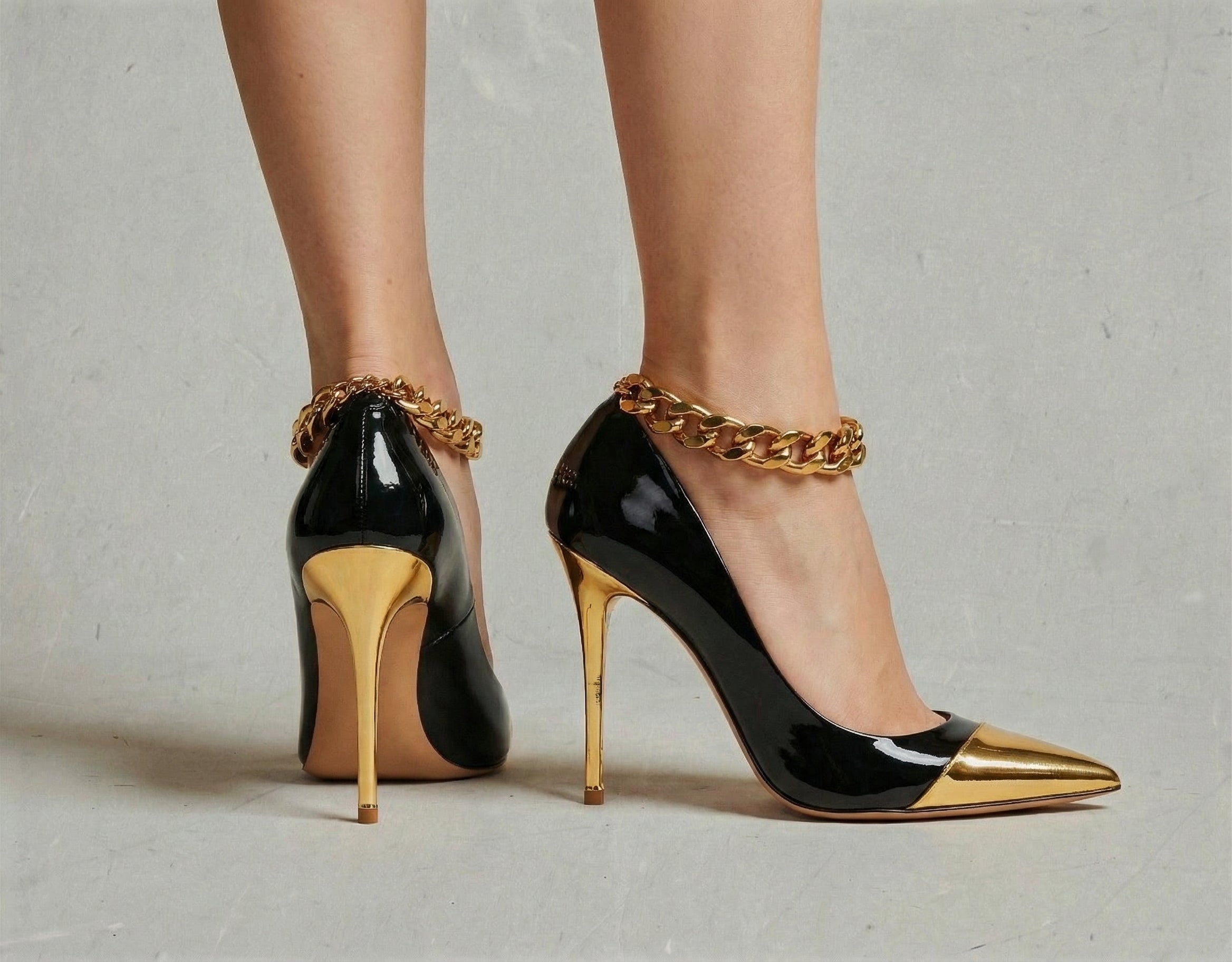 Black high-heeled shoes with gold accents and chain details on a neutral background