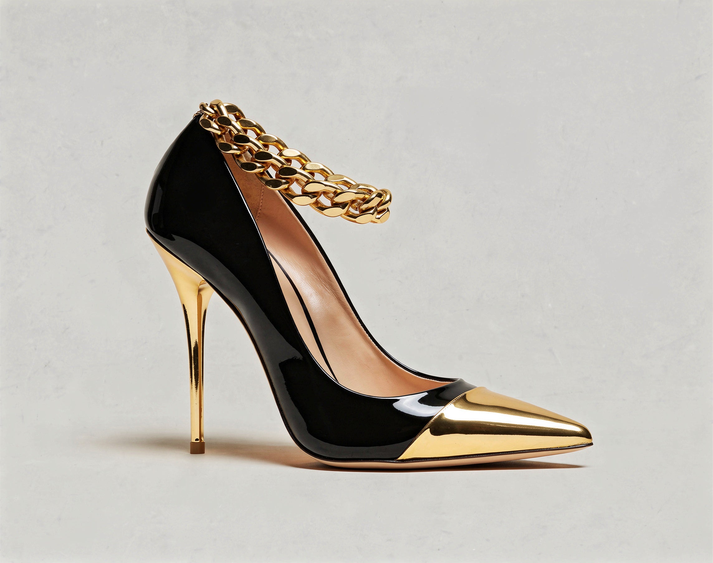Black high-heeled shoe with gold chain and heel on a light gray background